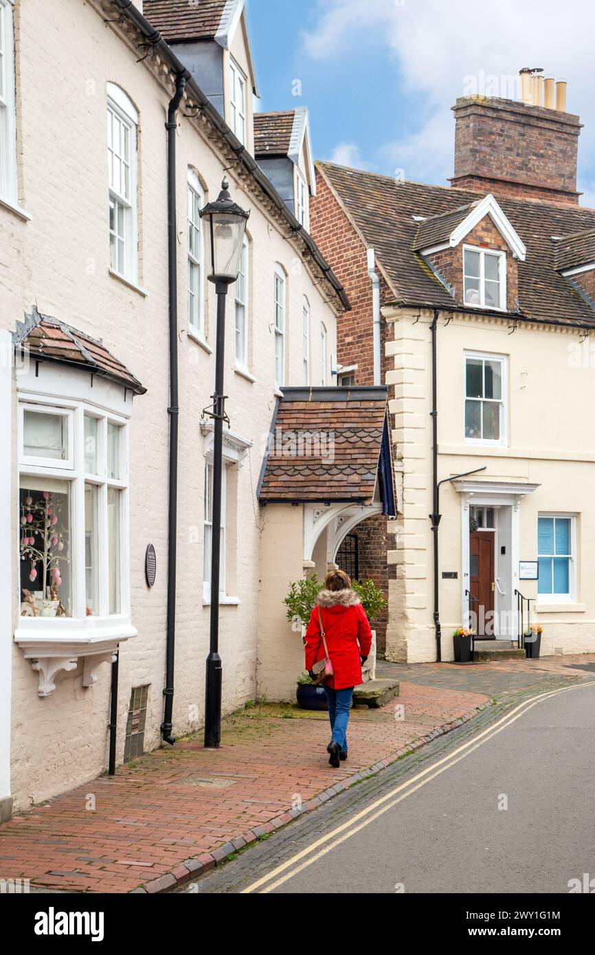 Woman in red coat walking  past houses and cottages along Eastcastle street in the Shropshire market town of Bridgnorth England UK Stock Photo