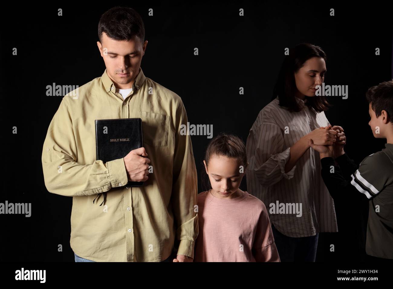 Family with Holy Bible praying together on dark background Stock Photo