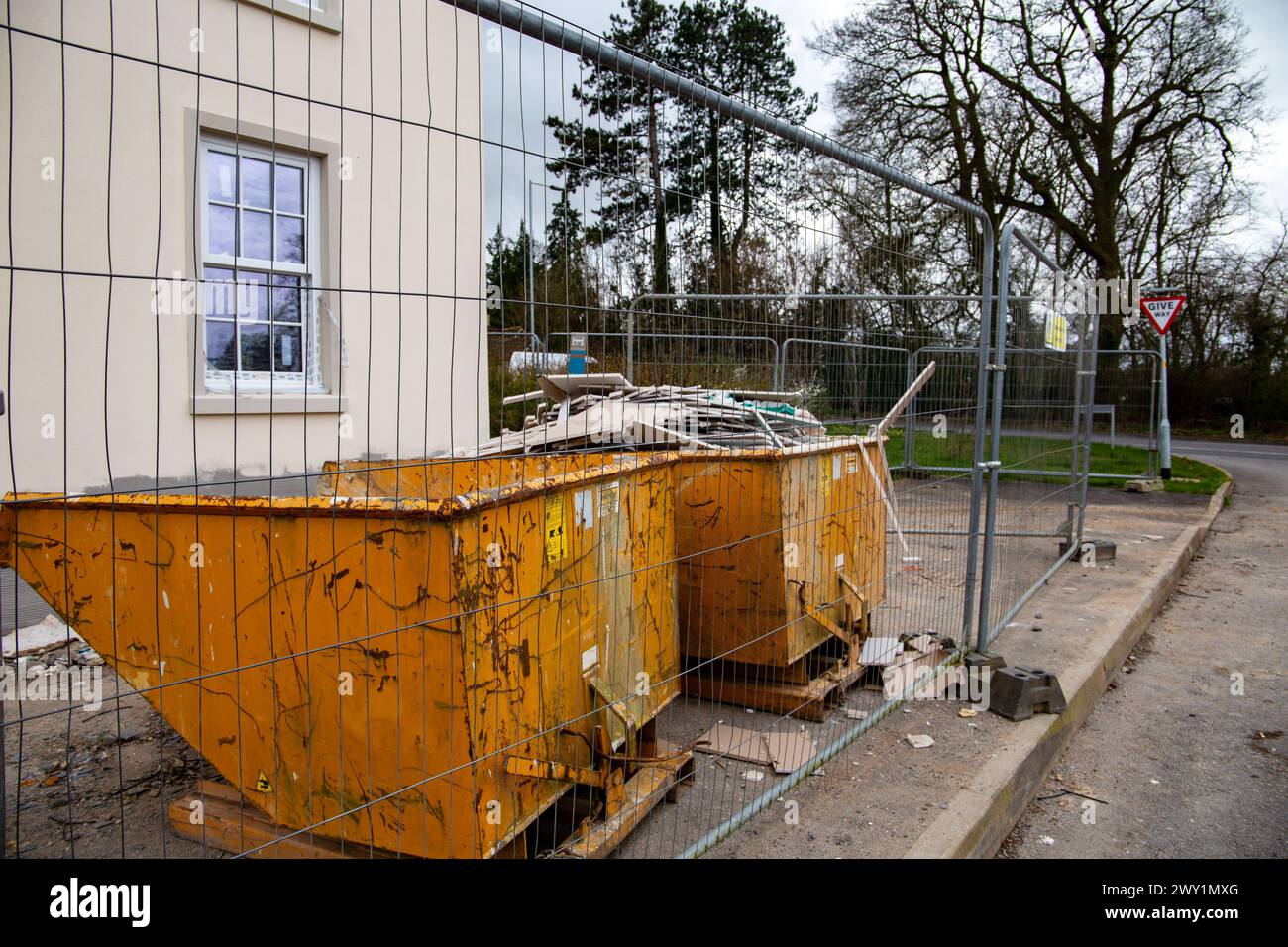 Two yellow rubbish garbage skips at a new build housing site one skip is full of plasterboard off cuts with with a safety fence around the site. Stock Photo