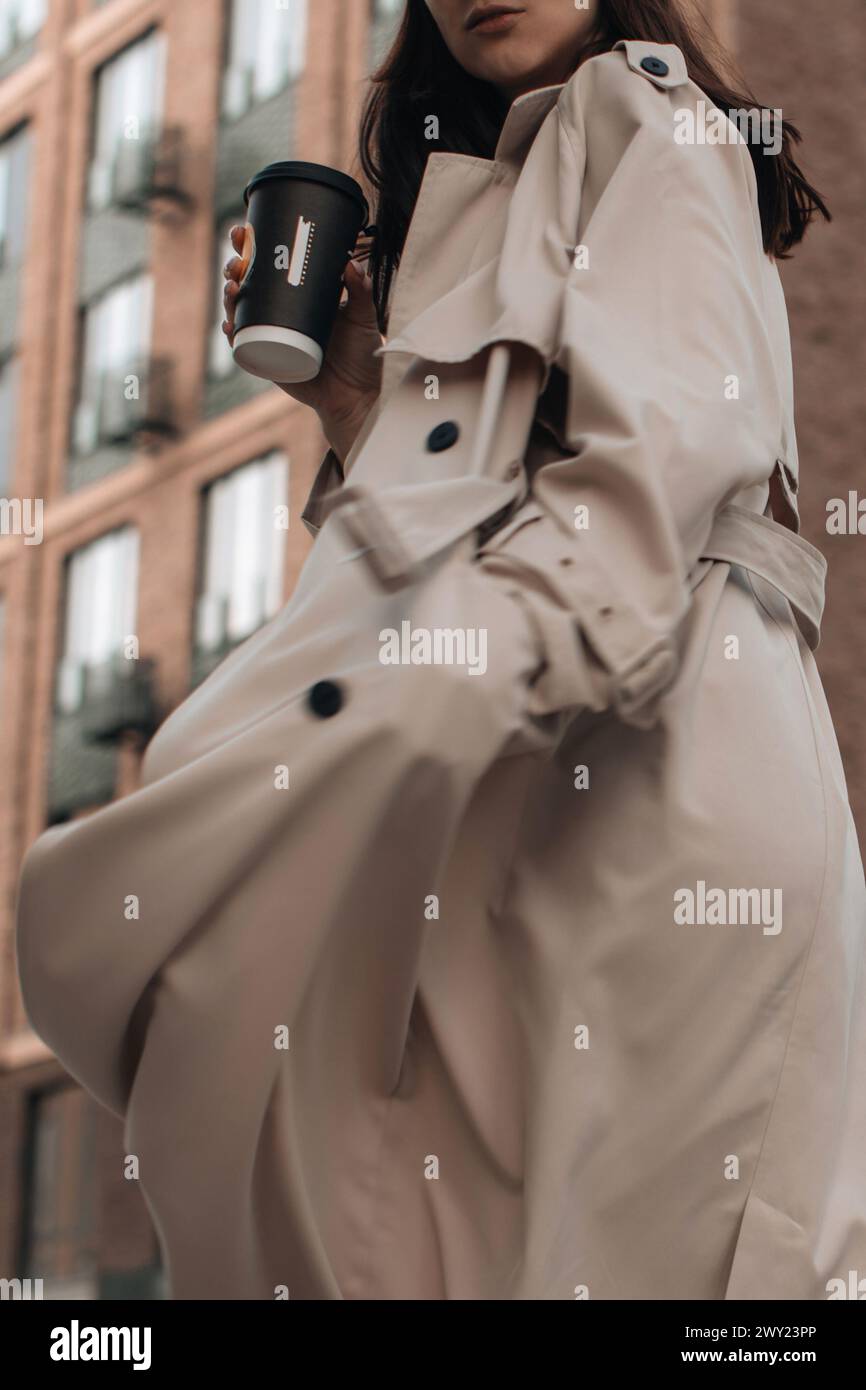 A young woman in a beige trench coat against the background of the city ...