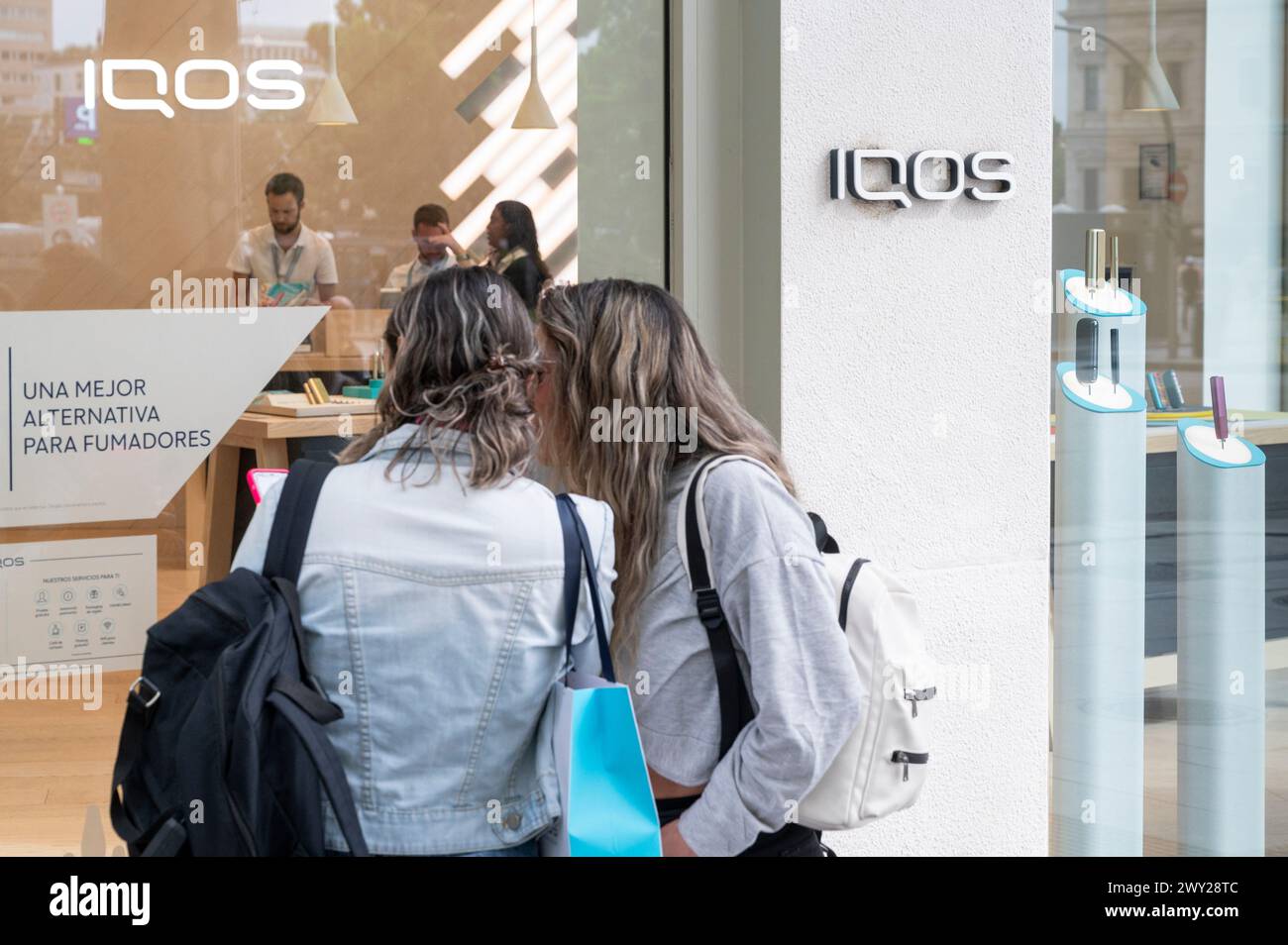 Shoppers window shop at the heated tobacco and electronic cigarette products brand and manufactured by Philip Morris International (PMI), IQOS, in Spain. Stock Photo