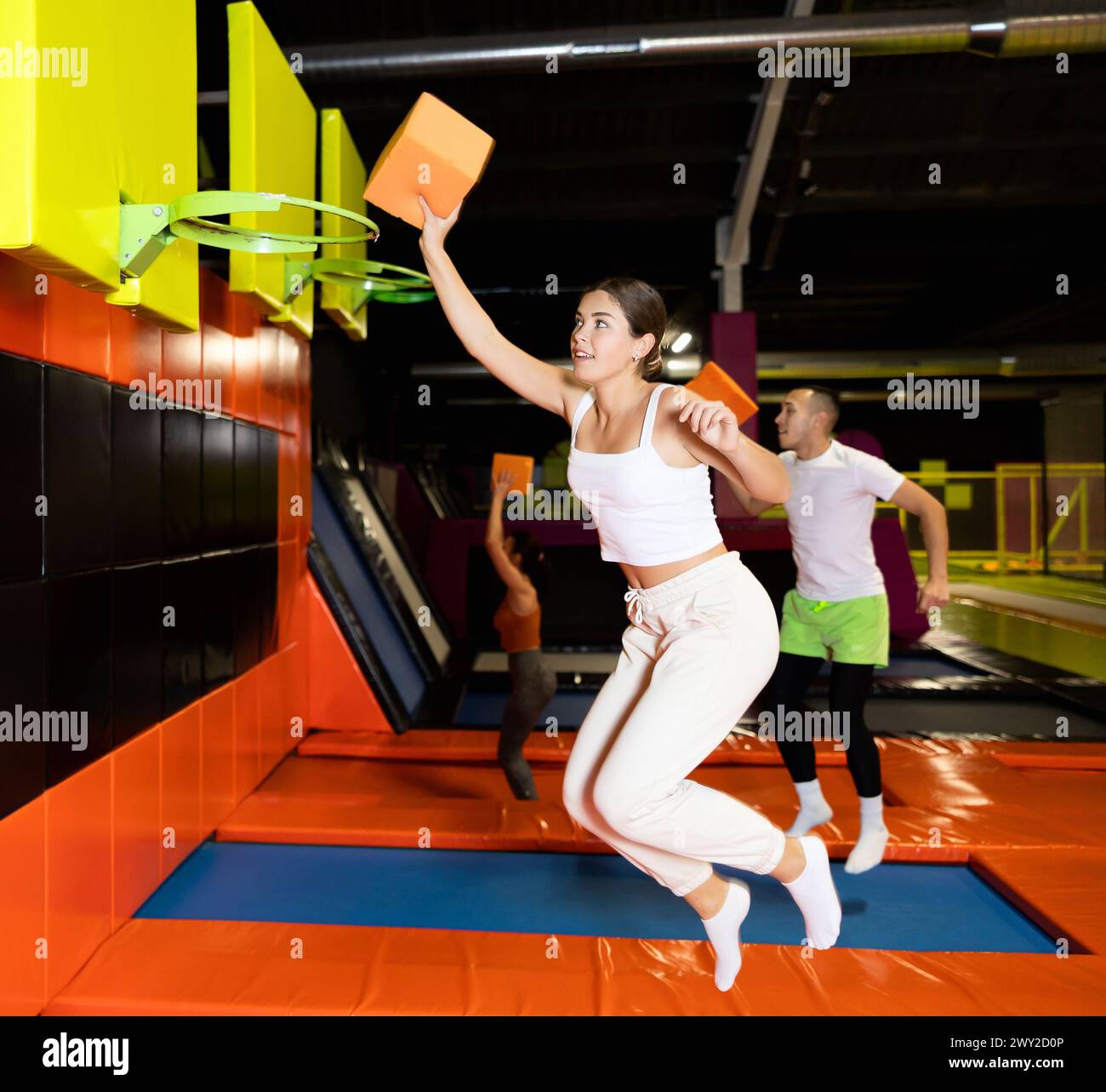 Athletic people throw ball into basketball basket while jumping on trampolines at an