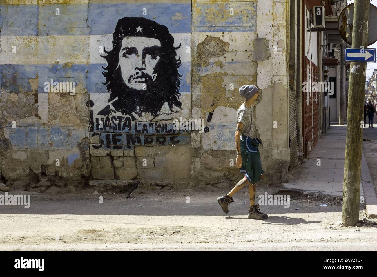 Slim Cuban man walks by an image of Che Guevara, Havana, Cuba Stock Photo