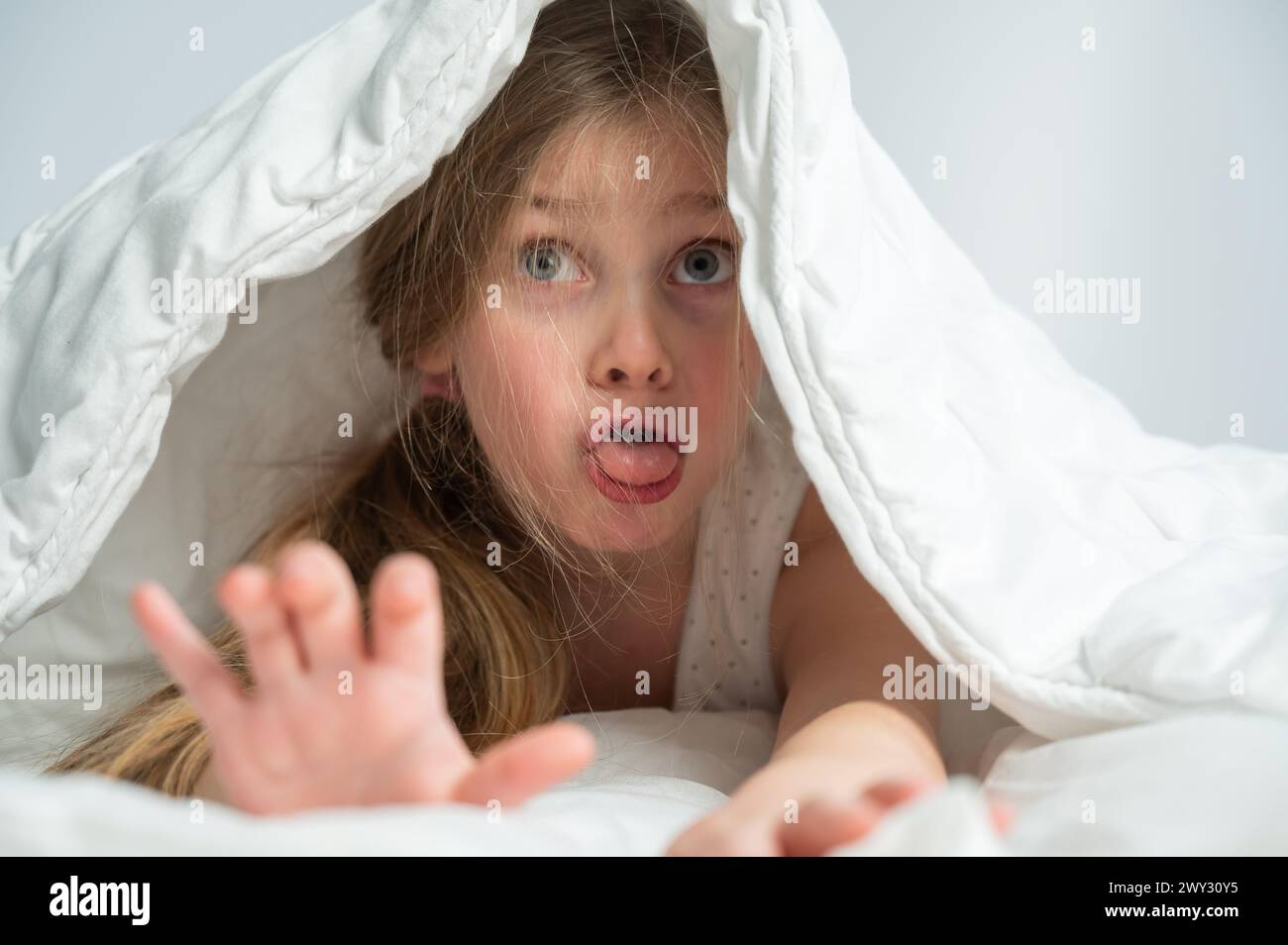 Portrait of a cute little girl laughing and hiding under the blanket
