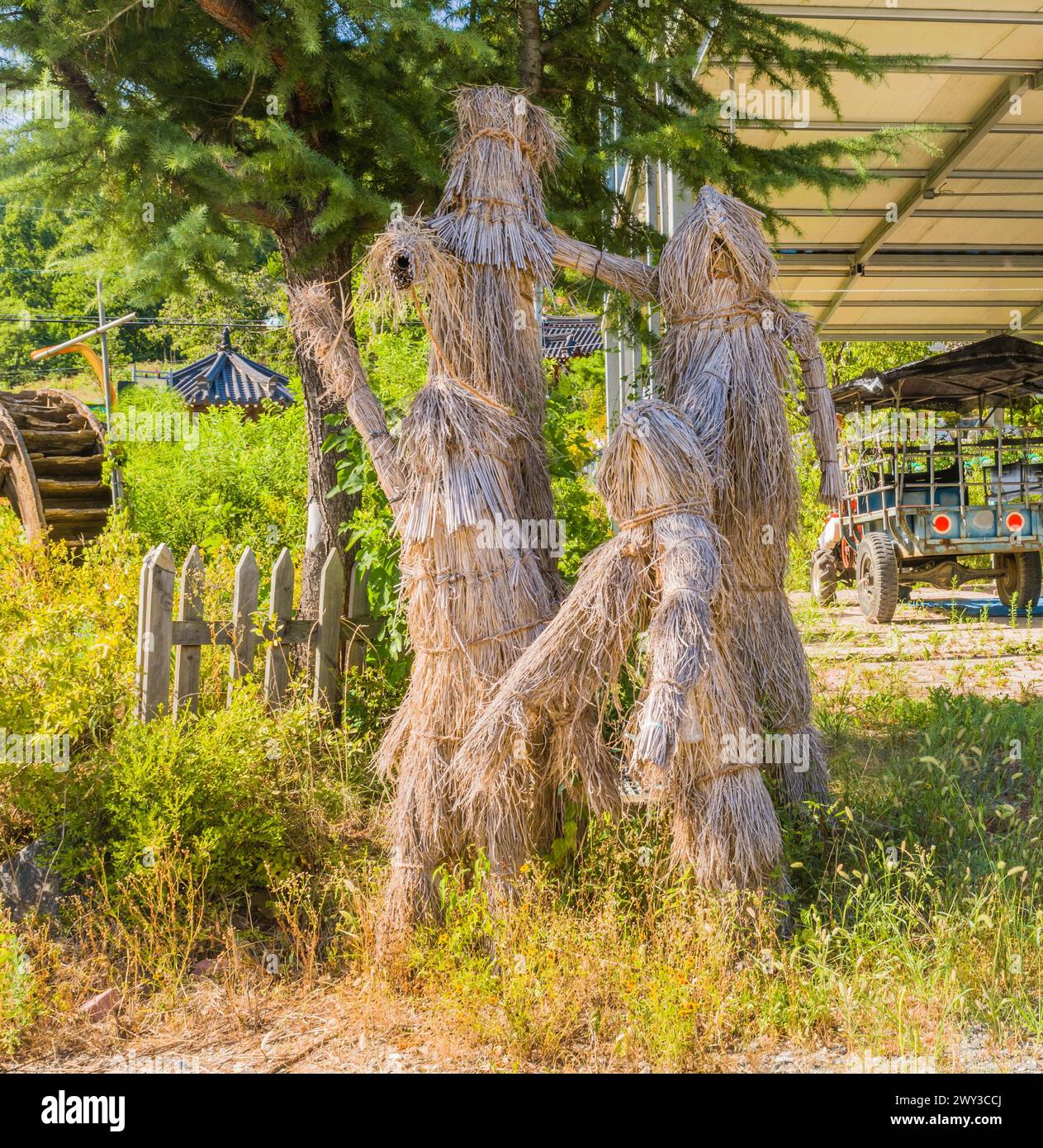 Family of people made out of straw and rope standing under pine tree on sunny day in rural community in South Korea Stock Photo