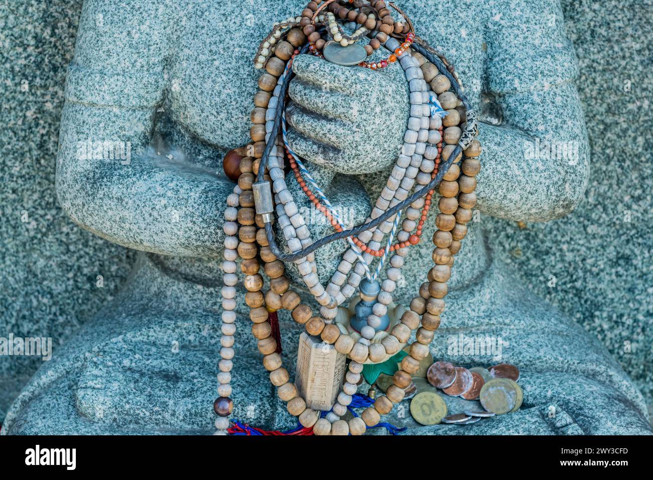 Closeup of prayer beads and coins left on seated rock carved Buddha in Yeongcheon, South Korea Stock Photo