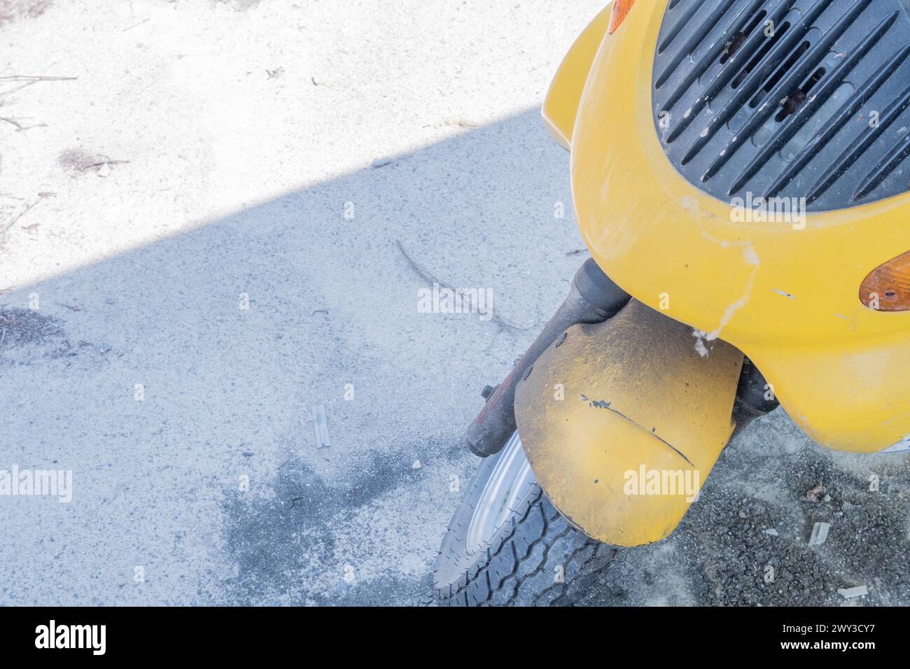 Front cowling and tire assembly of dirty yellow scooter parked in shade on sunny day in South Korea Stock Photo