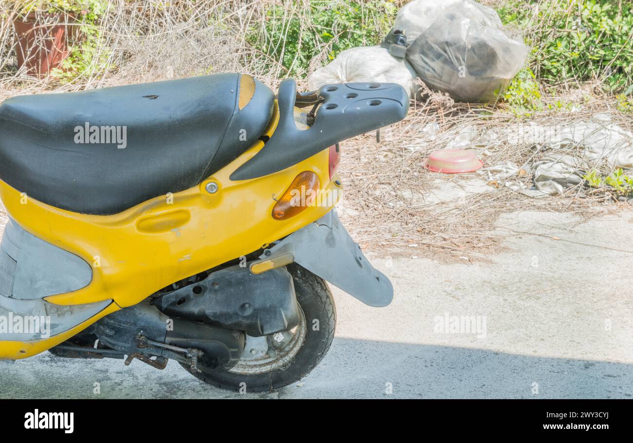 Seat and rear section of small yellow motor scooter parked on concrete with trash bag and high
