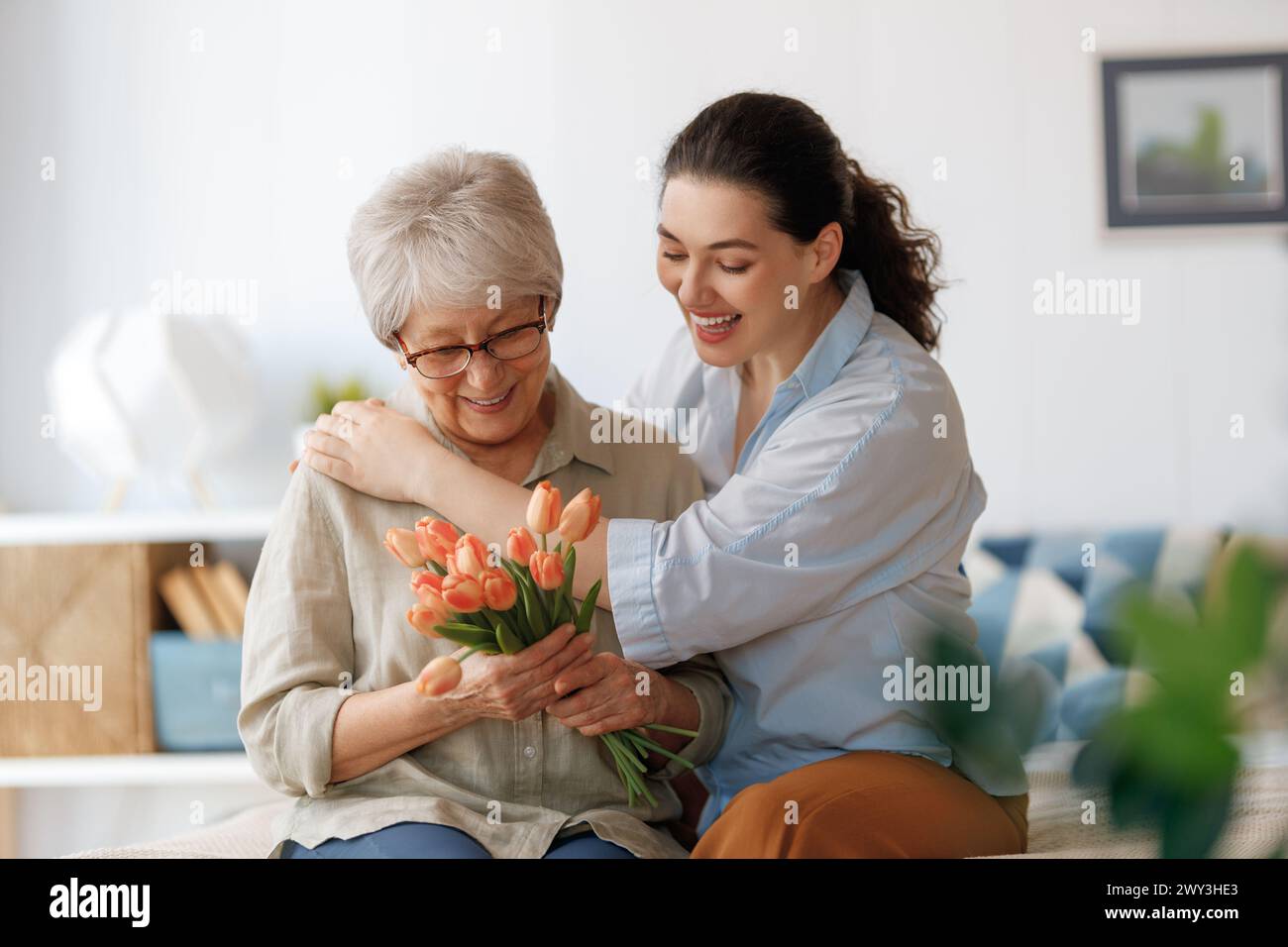 Beautiful young woman and her mother with flowers tulips in hands at home. Stock Photo