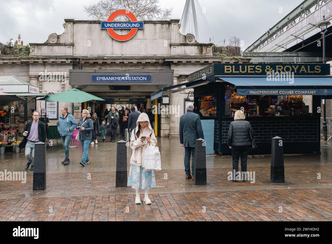 Embankment Station busy with commuters and tourists. A girl is checking her phone, perhaps checking directions to the next of London's attractions. Stock Photo