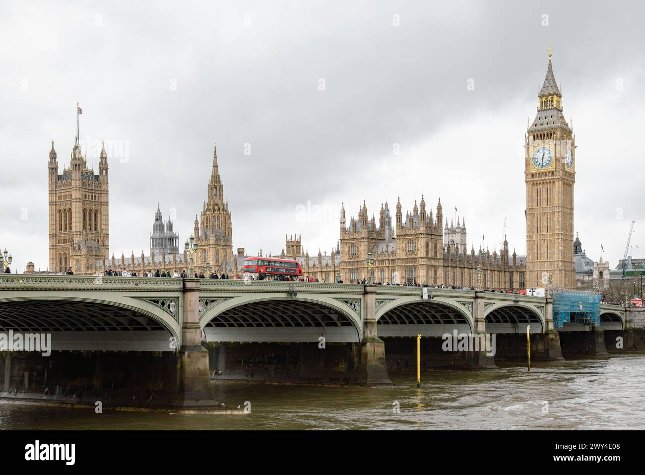 A red London bus crossing Westminster bridge. Behind it Big Ben and the Houses of Parliament, an iconic symbol of British democracy and heritage. Stock Photo