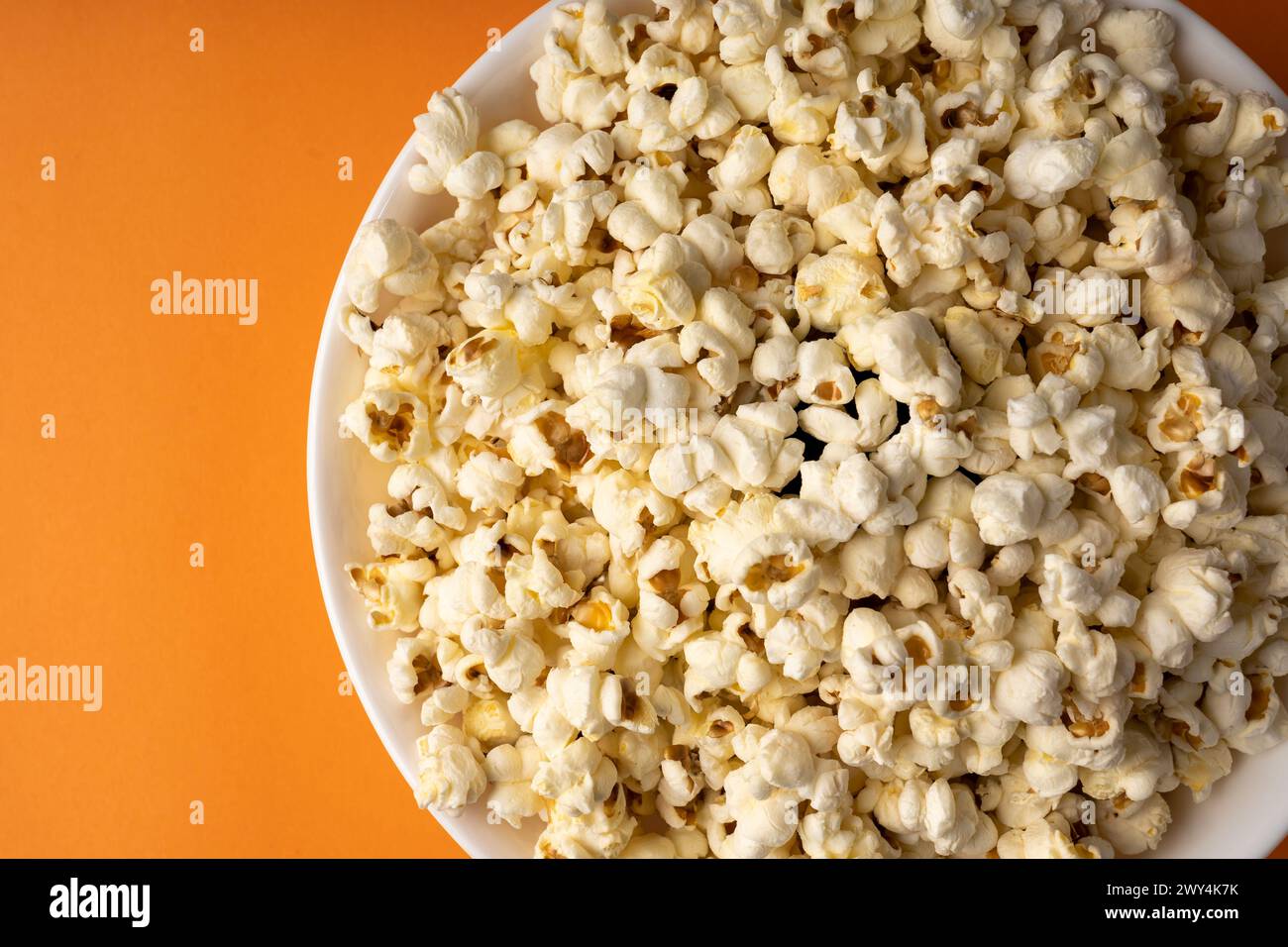 A white bowl of popcorn on an orange table. Stock Photo