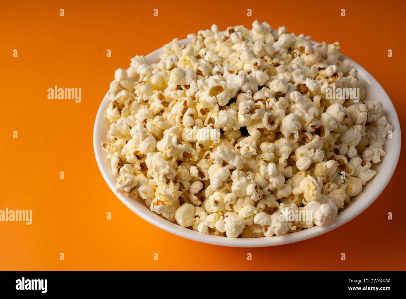 A white bowl of popcorn on an orange table. Stock Photo