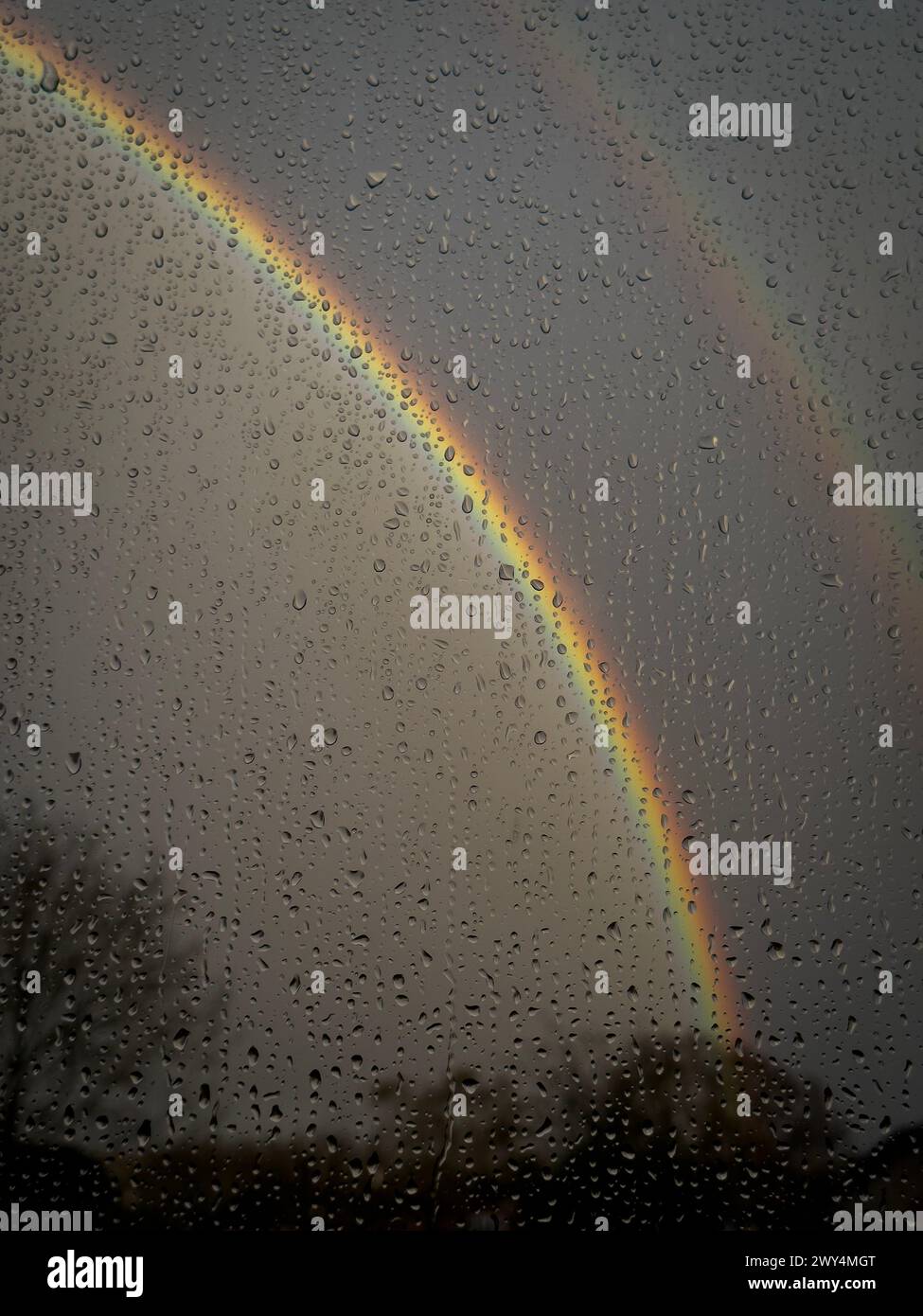 Raindrops on a window with an out of focus rainbow in a dark spring sky, Worcestershire, England. Stock Photo