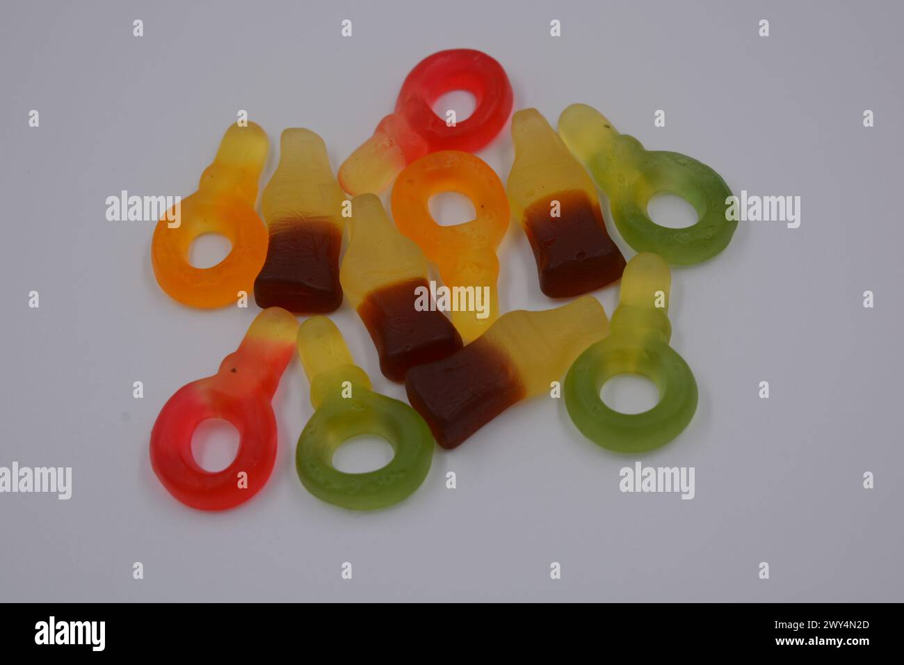 Beautiful and unusual candies. Yellow-green, red, brown, sweets in the form of a bottle of Coca-Cola, colored keys arranged on a white plastic backgro Stock Photo