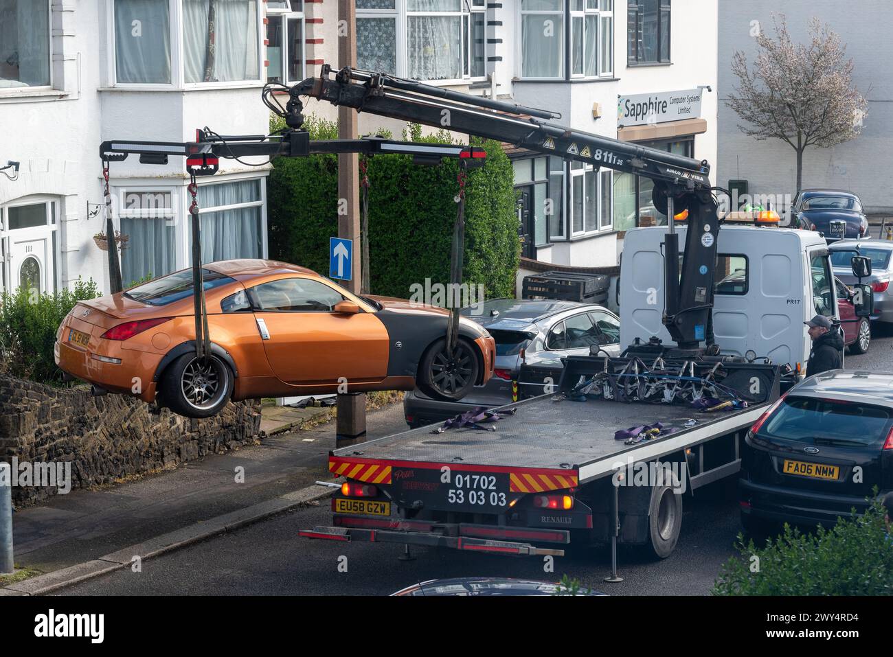 Damaged car being recovered by a breakdown truck in a confined narrow street, Essex, UK Stock Photo
