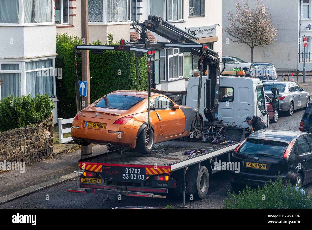 Damaged car being recovered by a breakdown truck in a confined narrow street, Essex, UK Stock Photo