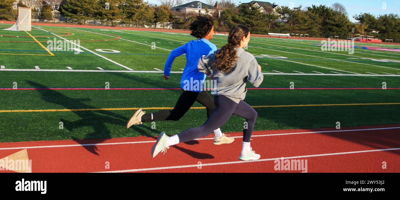 Two fast high school girls running fast on a track during practice on a sunny day in early spring. Stock Photo