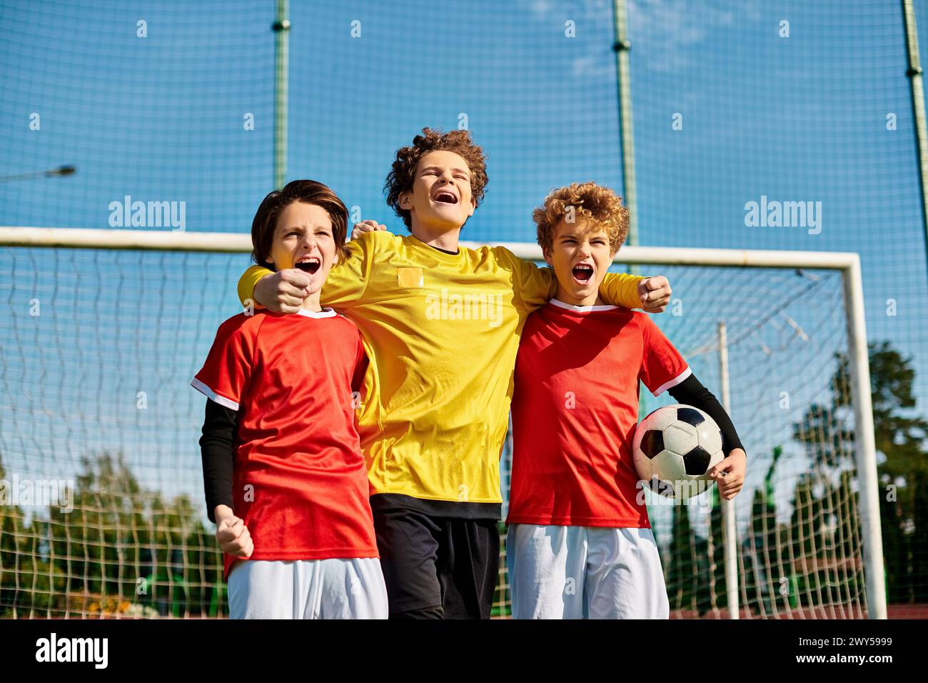 A group of young boys, all dressed in soccer jerseys, stand closely together in unity on a green soccer field. Each boy is looking in different direct Stock Photo