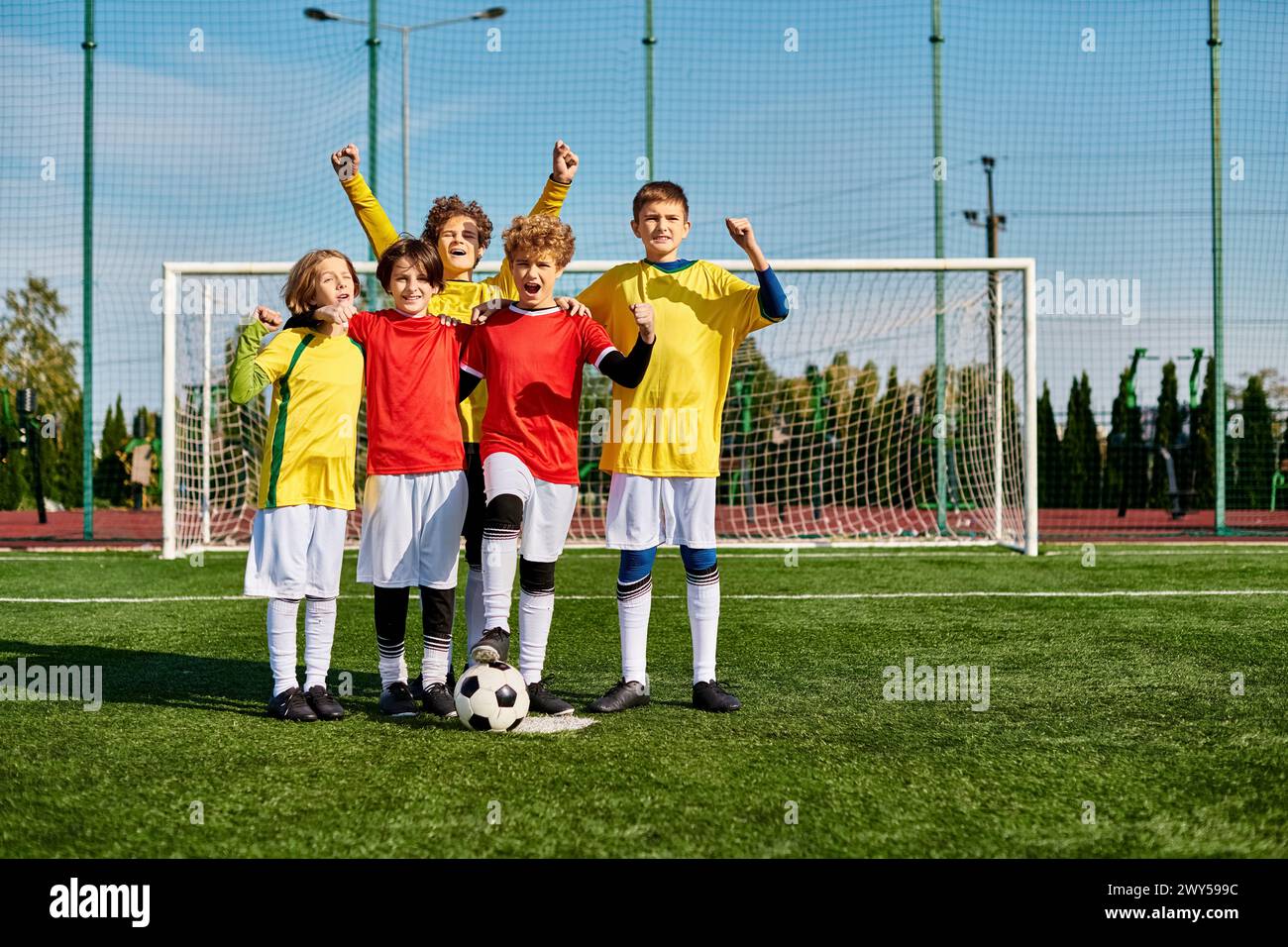 A group of young children, filled with energy and enthusiasm, stand triumphantly on top of a soccer field, celebrating their teamwork and victory. Stock Photo