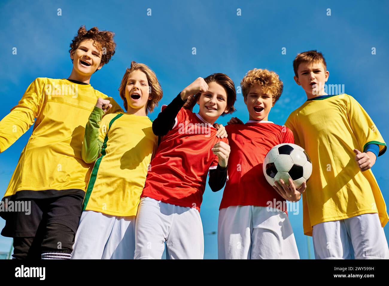 A lively group of young individuals stand closely together, holding a soccer ball with enthusiasm and camaraderie. Their faces reflect excitement and Stock Photo