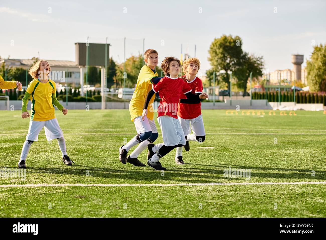 A vibrant scene unfolds as a group of energetic young children engage in a game of soccer on a grassy field. Dressed in colorful jerseys, they dribble Stock Photo