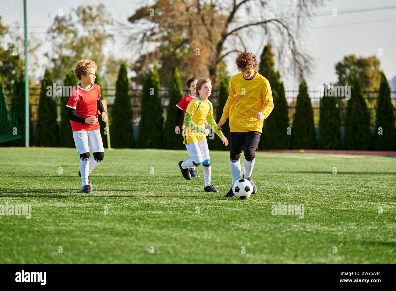 A lively group of young children joyfully playing a game of soccer on a green field. They are running, kicking the ball, and shouting with excitement Stock Photo