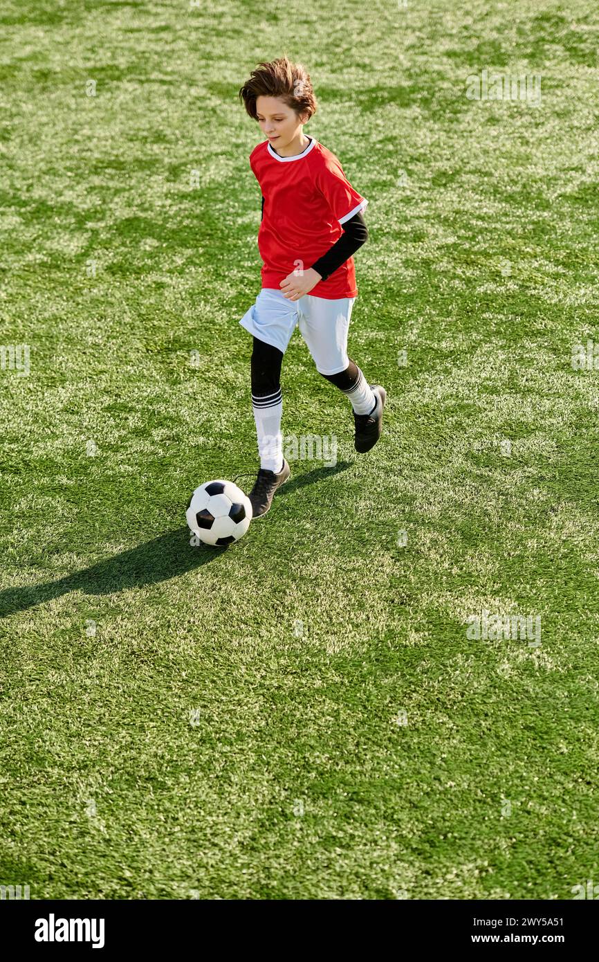 A young boy kicks a soccer ball with determination and skill on a lush green field, showcasing his passion for the sport. Stock Photo