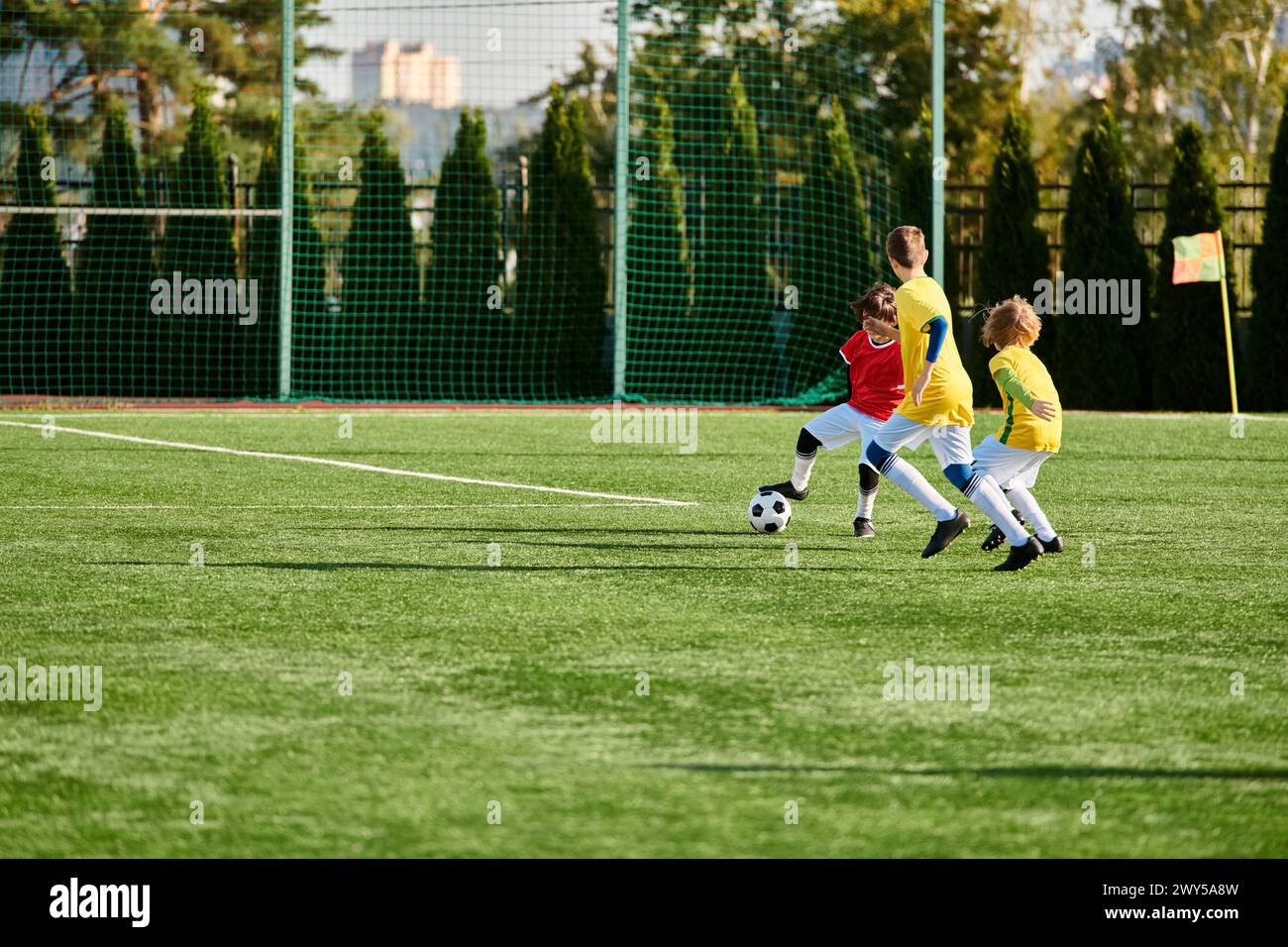 A lively group of young children play a game of soccer, running and kicking the ball across the field with beaming smiles and competitive spirit. Stock Photo