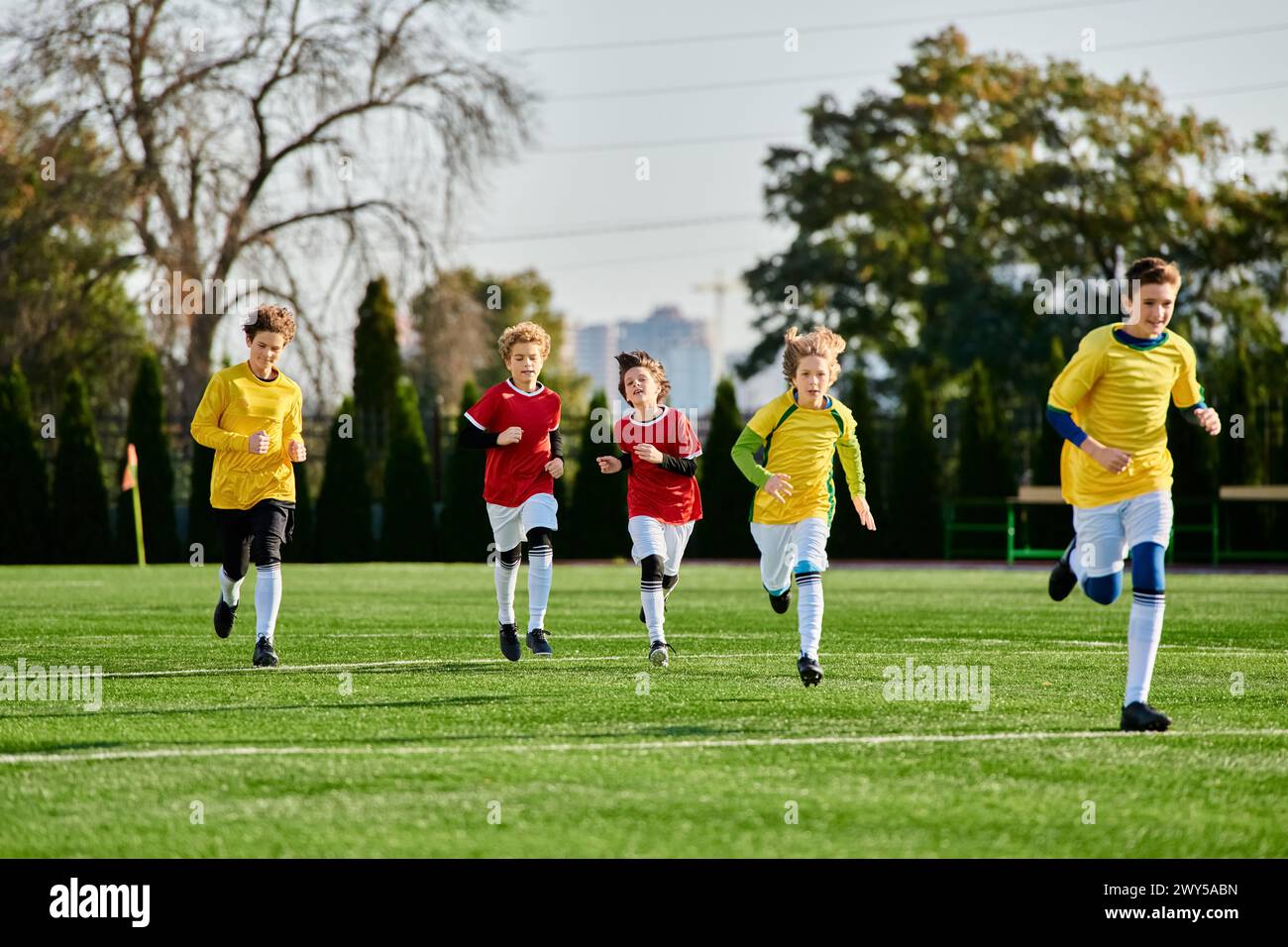 A group of diverse young children, clad in colorful jerseys, play soccer on a sun-drenched field, kicking the ball, running and laughing in camaraderi Stock Photo