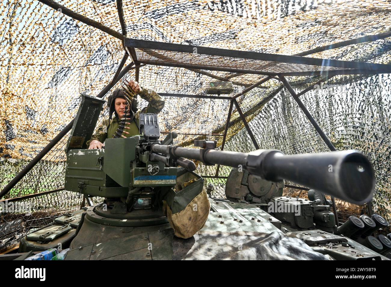 UKRAINE - MARCH 31, 2024 - A serviceman of the 1st Tank Brigade of the Ukrainian Ground Force holds an ammunition belt on a tank, Ukraine. Stock Photo