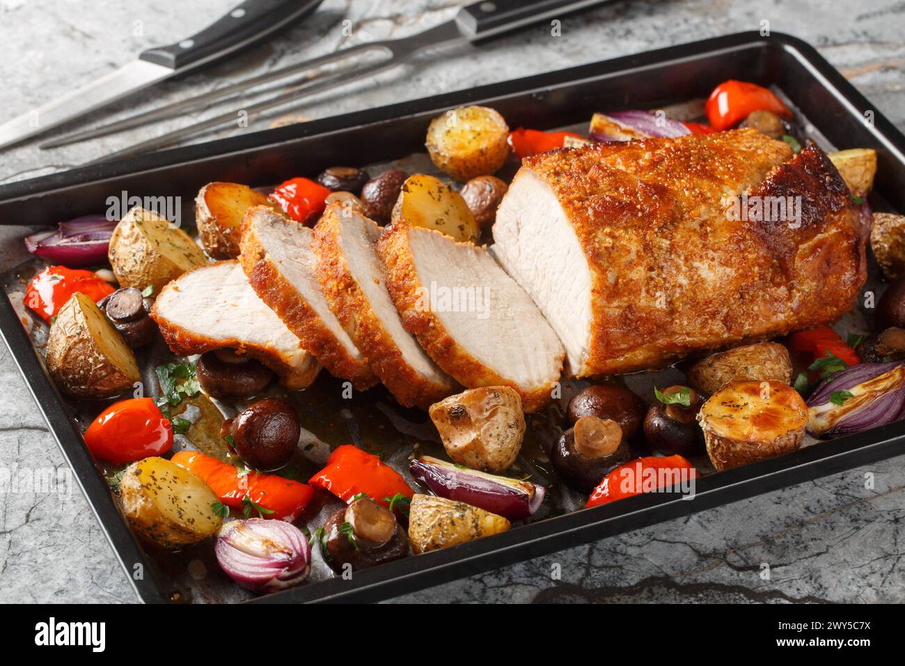 Delicious festive baked pork loin with vegetables and mushrooms close-up on a baking sheet on the table. Horizontal Stock Photo