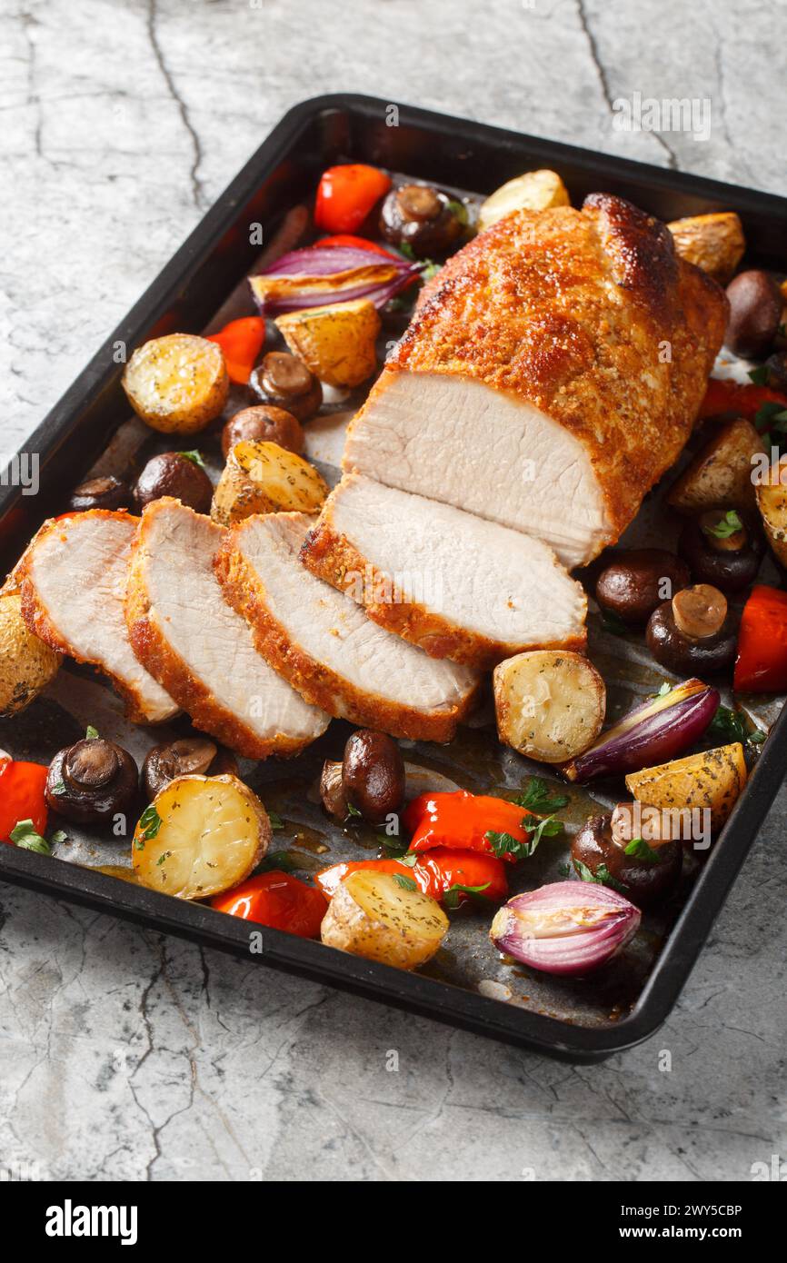 Flavor boosted pork loin baked together with potatoes, peppers, mushrooms and onions closeup on a baking sheet on the table. Vertical Stock Photo
