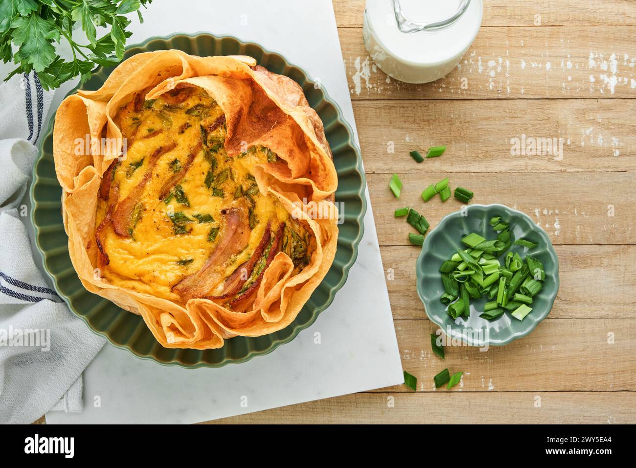 Homemade quiche or tart with slices of bacon and leeks with tortilla instead of dough on wooden cutting board on rustic old wooden background. Quiche Stock Photo