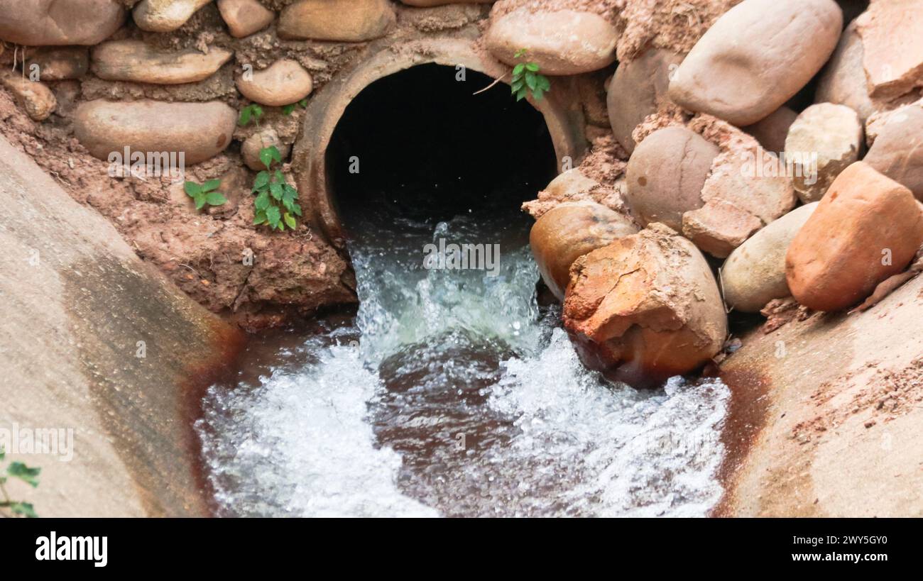 Water flowing out of concrete pipe in concrete canal surrounding with ...