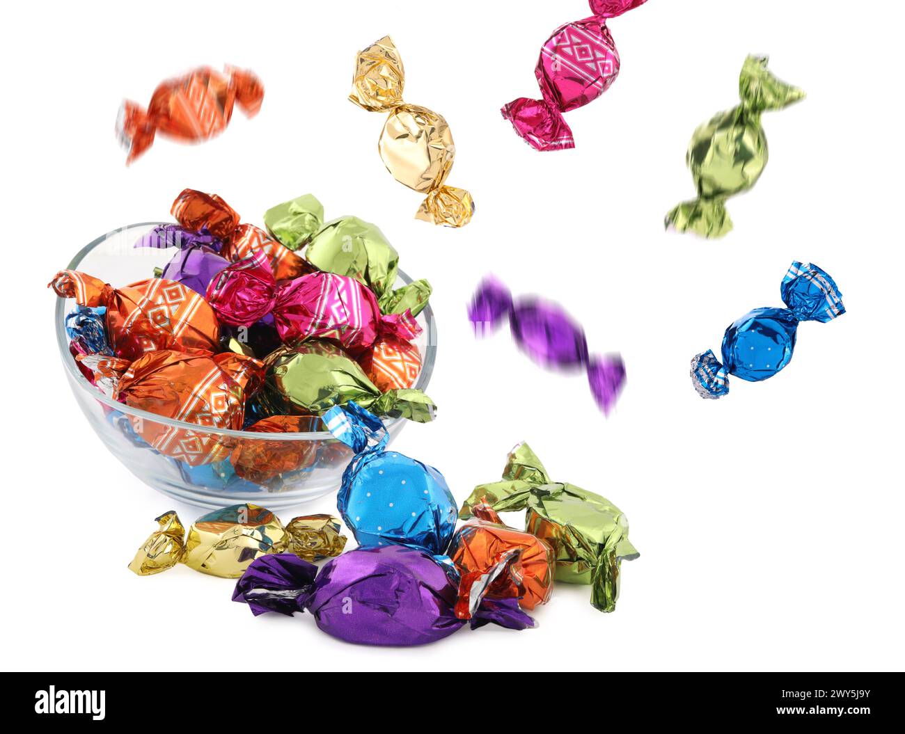 Candies in bright wrappers falling over bowl on white background Stock Photo