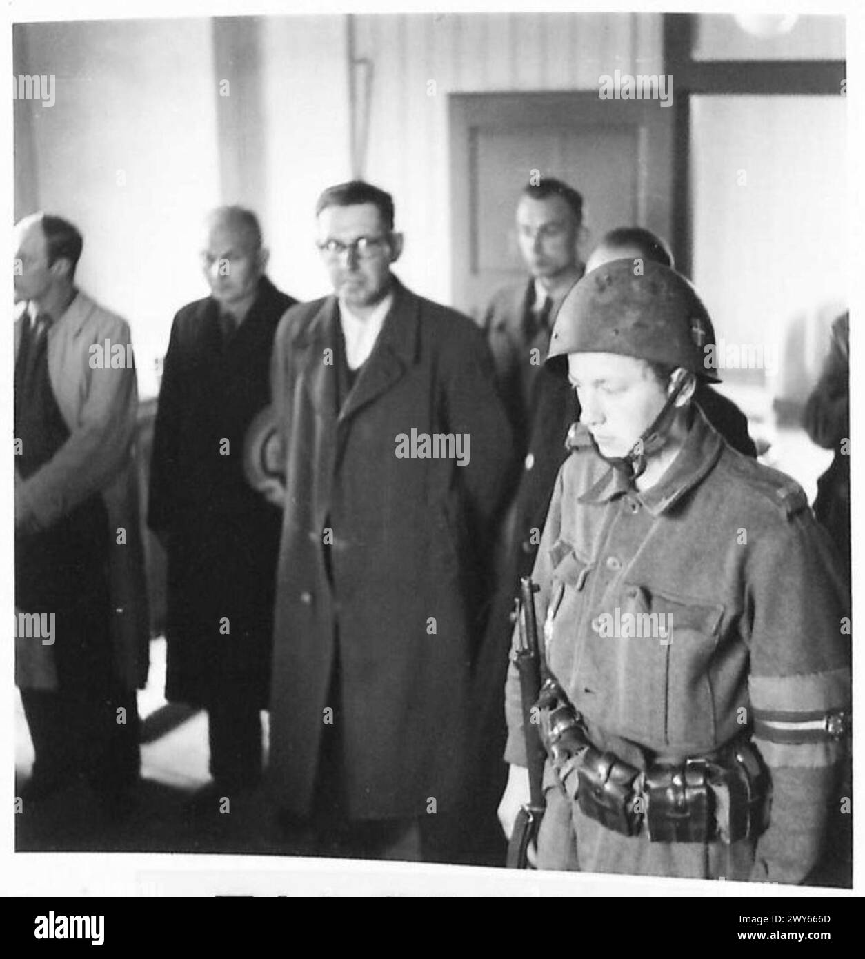 THE GREAT ROUND-UP - Captured Gestapo Agents are lined up inside the Interrogation Room - a Danish soldier stands guard. , British Army, 21st Army Group Stock Photo
