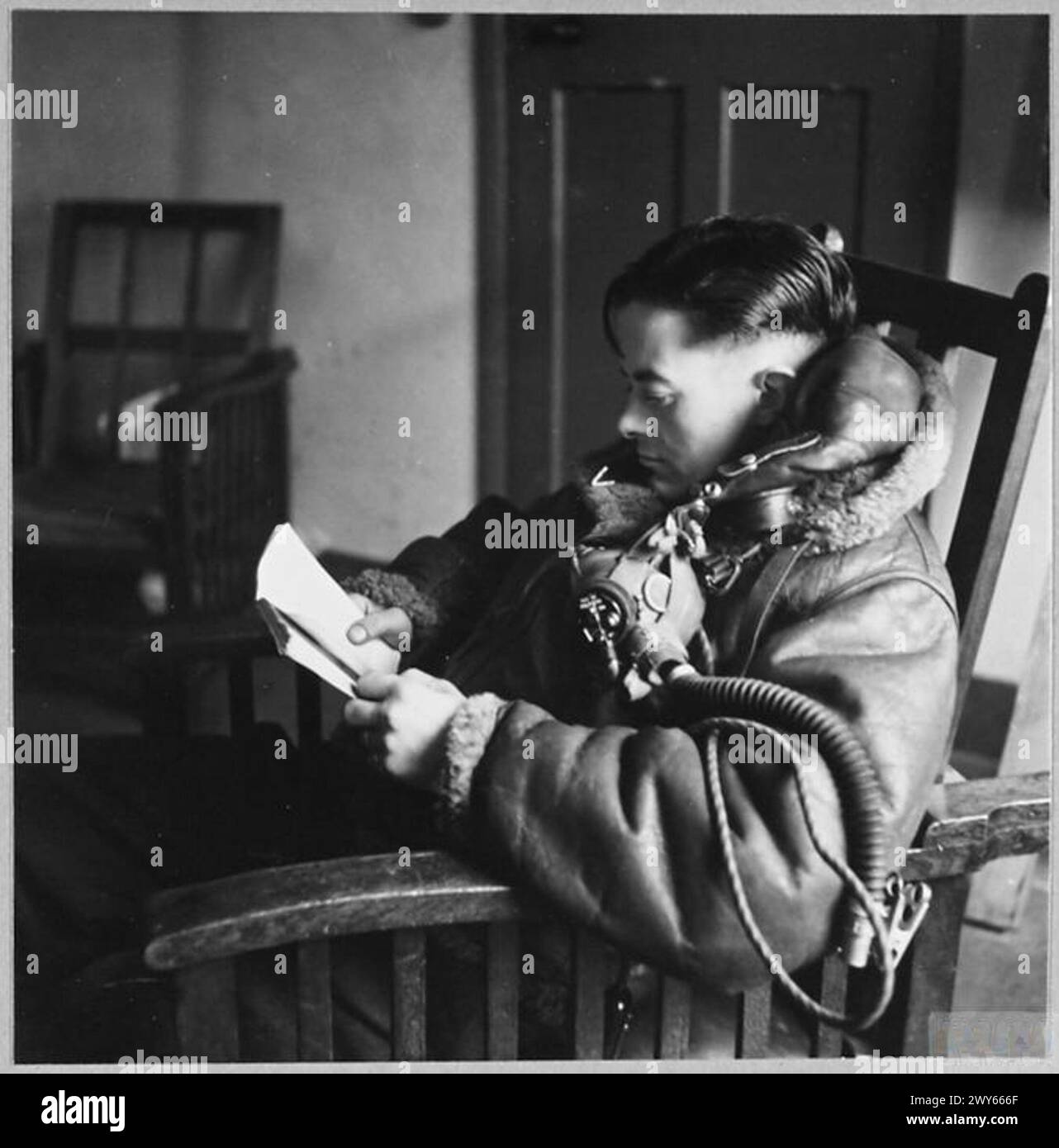 'BOMBER BOYS' ARE AVID READERS WHILE AWAITING BRIEFINGS. - Picture issued 1942. With the massive wheel of a Lancaster's undercarriage as a substantial back rest, a member of the ground crew tries to keep abreast with his reading. , Royal Air Force Stock Photo