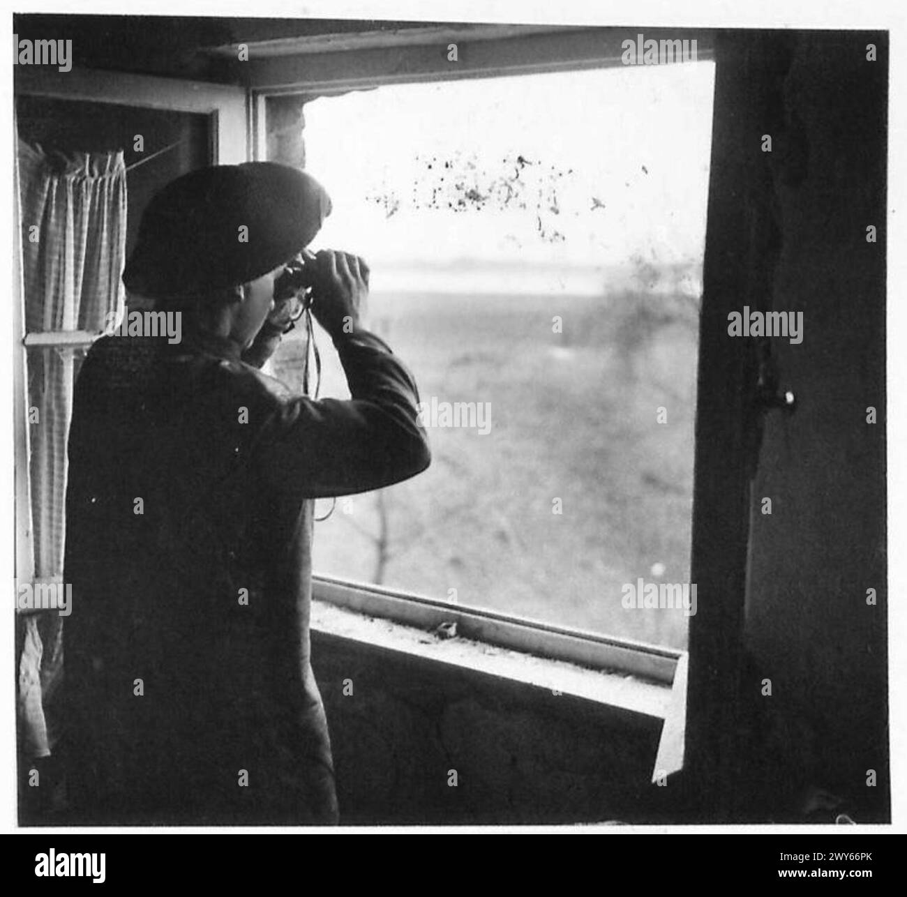 OVERLOOKING THE RHINE - Pte Loenard Webb of the SLI watches for movement on the far bank of the Rhine. The Rhine can be seen from the window. , British Army, 21st Army Group Stock Photo