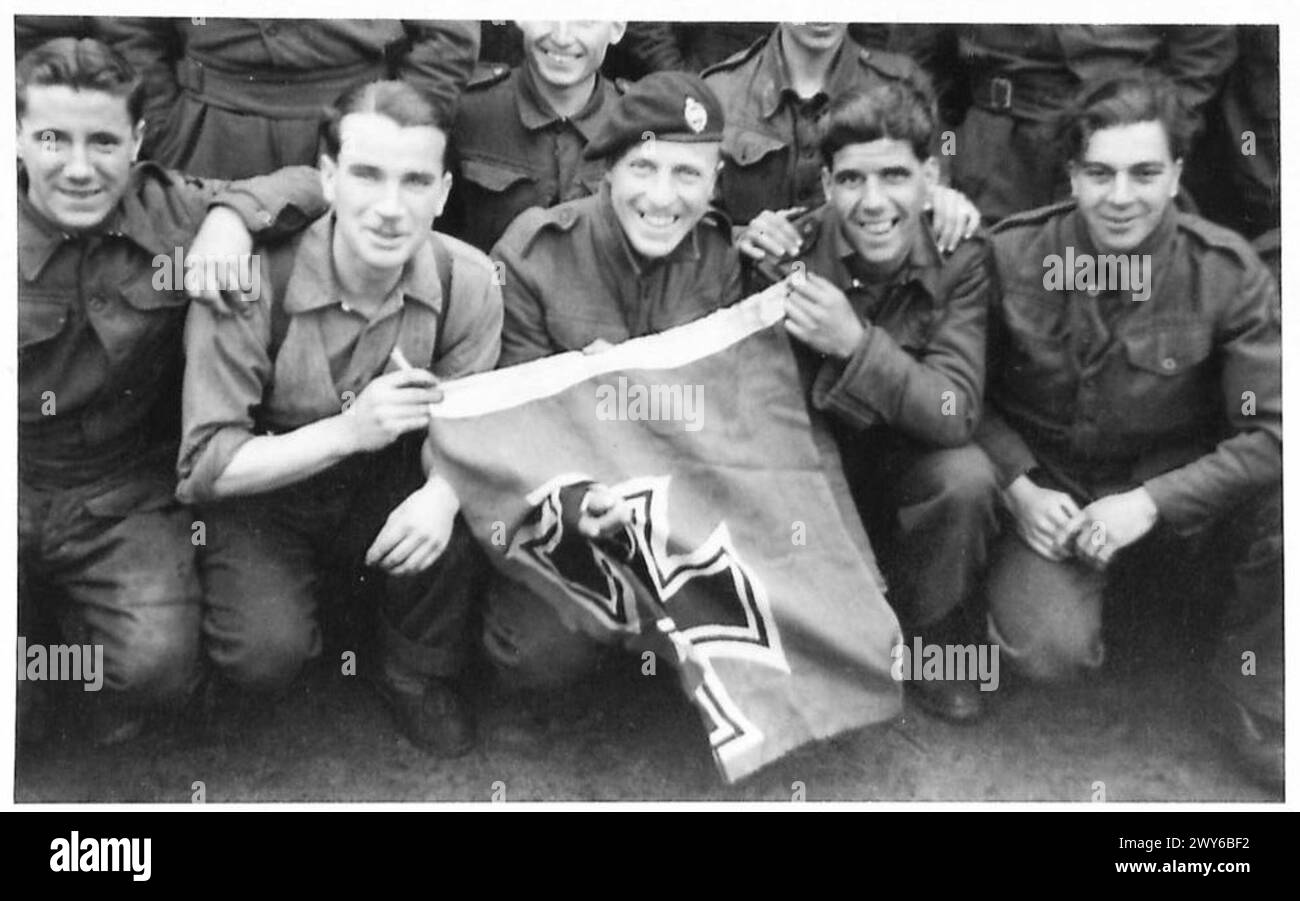 BRITISH TROOPS OVERRUN NEW P.O.W. & POLITICAL PRISONER CAMP AT SANDBOSTEL - British P.O.W., Tpr. J. Fletcher of The Vine, Branton, Doncaster, gives the 'V' sign through a town swastika flag. He was with 1st Royal Tank Regiment and taken prisoner five weeks ago at Sudlo seen with other released P.O.W. , British Army, 21st Army Group Stock Photo