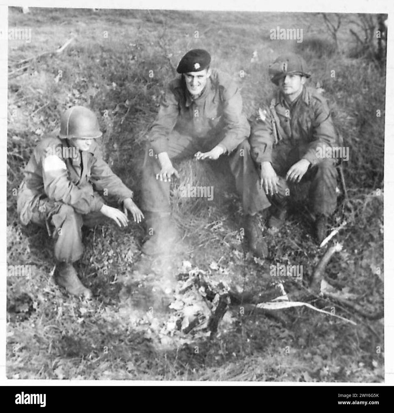 11TH ARMOURED DIVISION SPEARHEAD - A British guardsman shares a fire with American Paratroopers Left to right - 1st Class Rudy Paratroopers [of Newark New Jersey] 17th U.S.Airborne Division Gdsm. W.Angus of Aberdeen, Scots Guards, and Sgt.Harry Staughton of Richmond, Virginia - 17th U.S. Airborne Division. , British Army, 21st Army Group Stock Photo