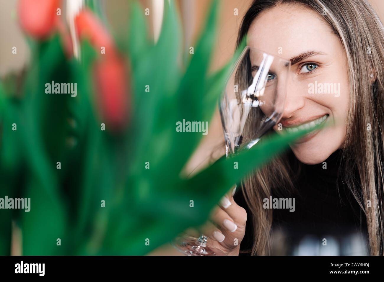 Happy woman looking at camera through glass wine glass while holding it in hand Stock Photo