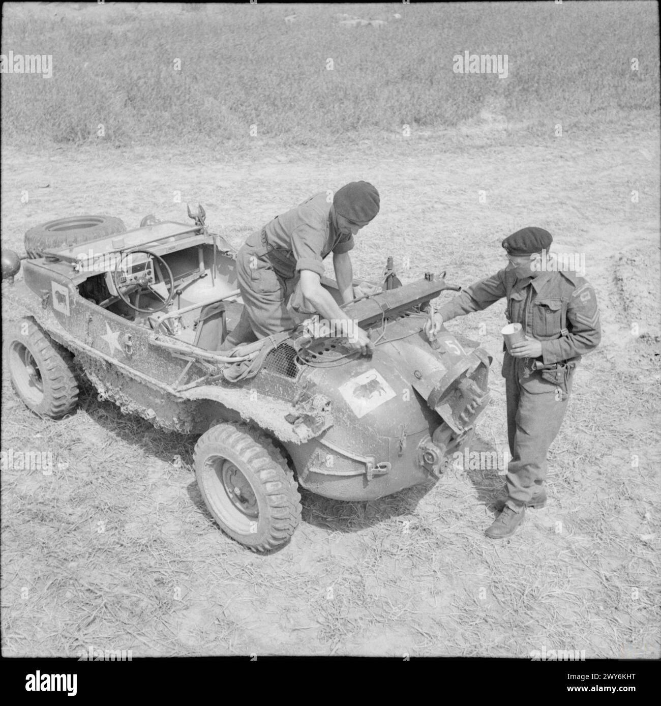 THE BRITISH ARMY IN NORMANDY 1944 - Men of 23rd Hussars, 11th Armoured Division, painting divisional and arm of service markings on a German Schwimmwagen captured from 12th SS Panzer Division (HitlerJugend), 6 July 1944. , British Army, 21st Hussars, British Army, 11th Armoured Division Stock Photo