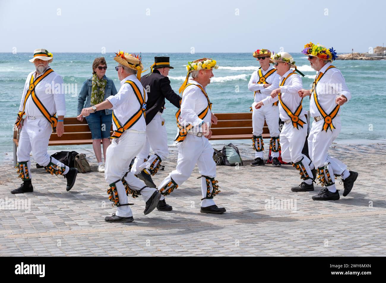 A group of touring British morris men or dancers dancing in the Old Harbour area of Paphos, Cyprus. the group are dressed in white with straw hats Stock Photo