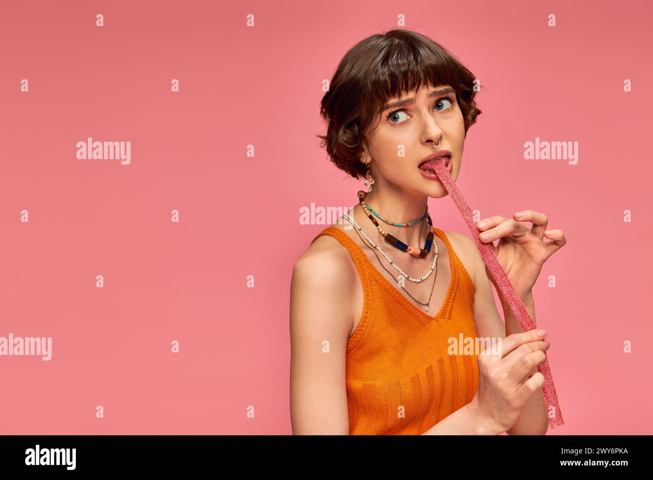 pretty girl in 20s with nose piercing and white teeth biting sweet and sour candy stripe, pink set Stock Photo