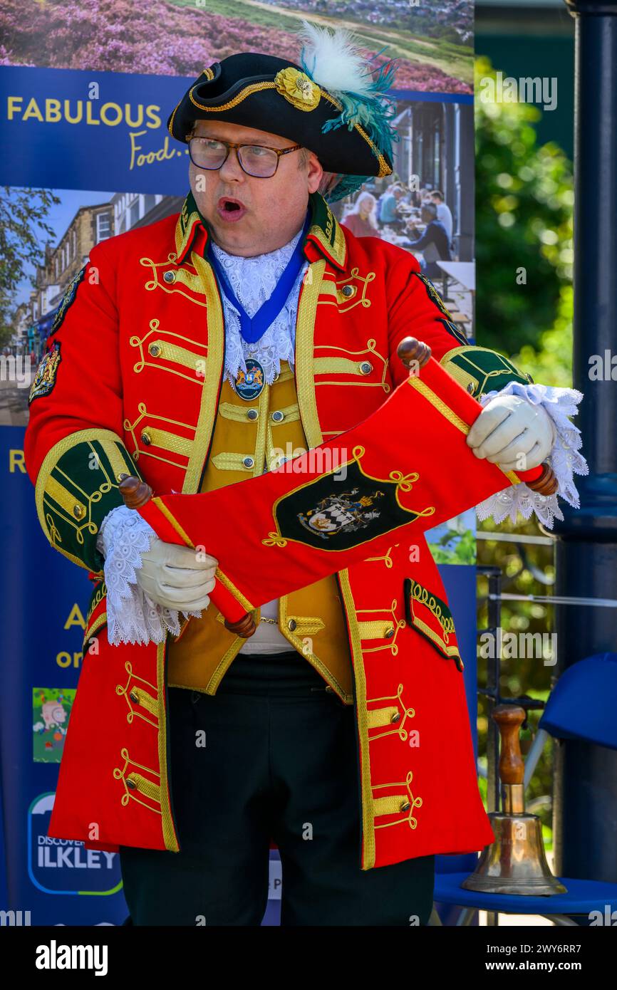 Male town crier (colourful braided crier's uniform) proclaiming, making loud public proclamation & announcement - Ilkley, West Yorkshire, England UK. Stock Photo