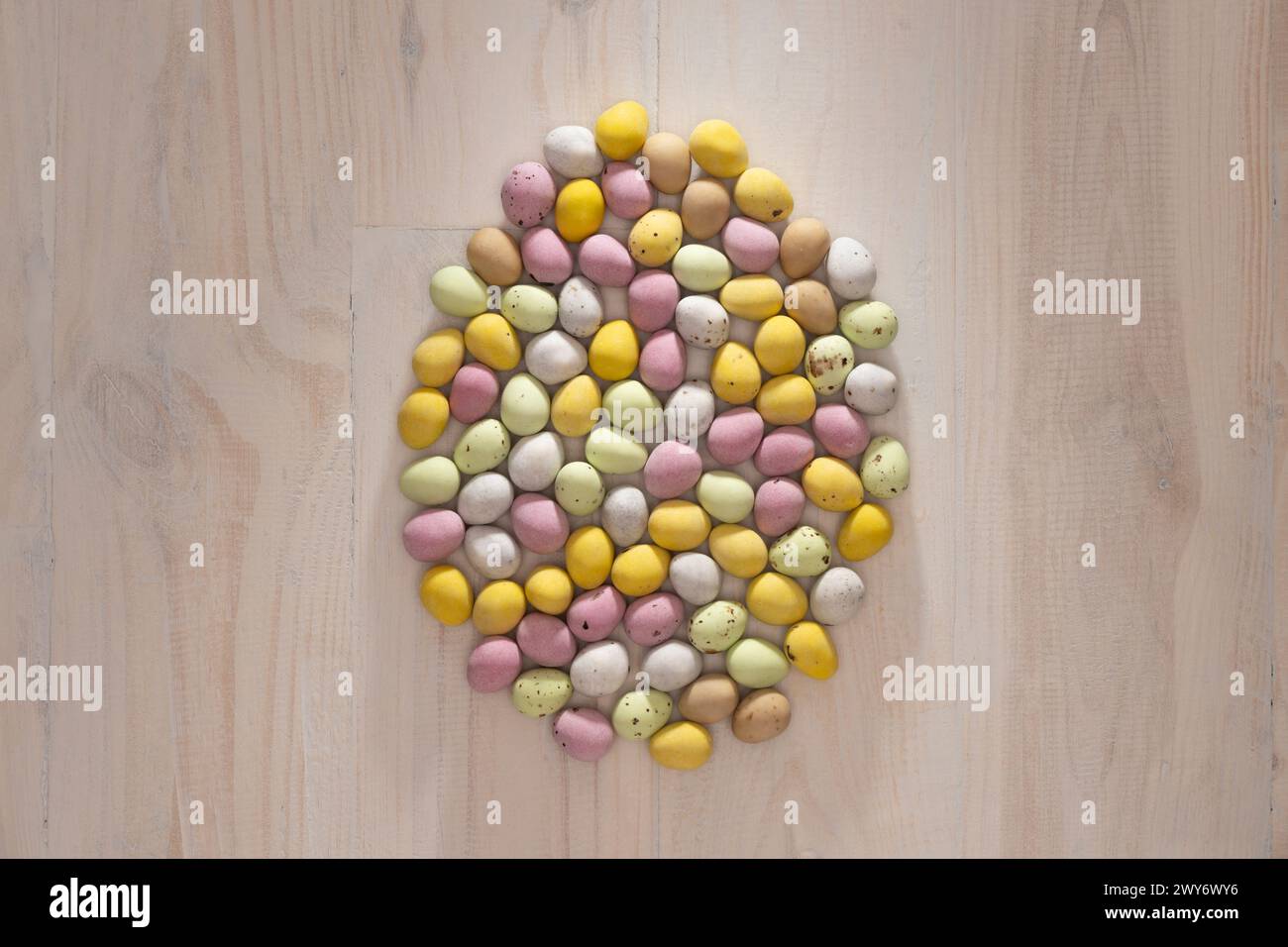Sugar-coated mini eggs, in pastel colours, arranged in an egg shape on a wooden background. Stock Photo