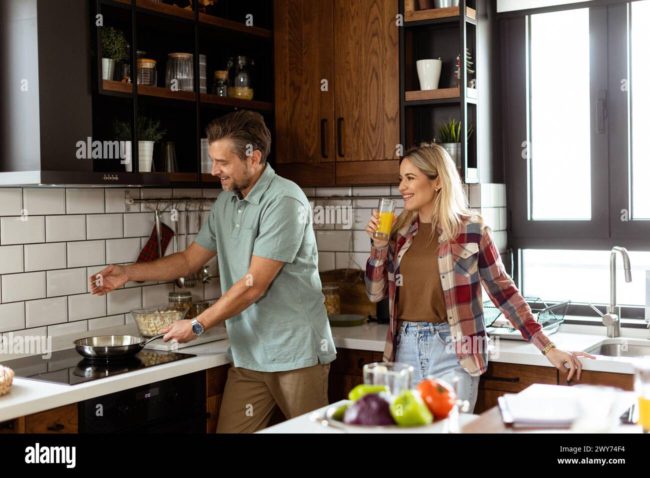A man and woman sharing a laugh as they cook in a cozy, well-organized kitchen Stock Photo