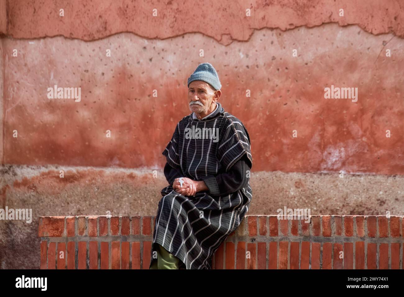 A man seated on a brick bench by graffiti wall Stock Photo
