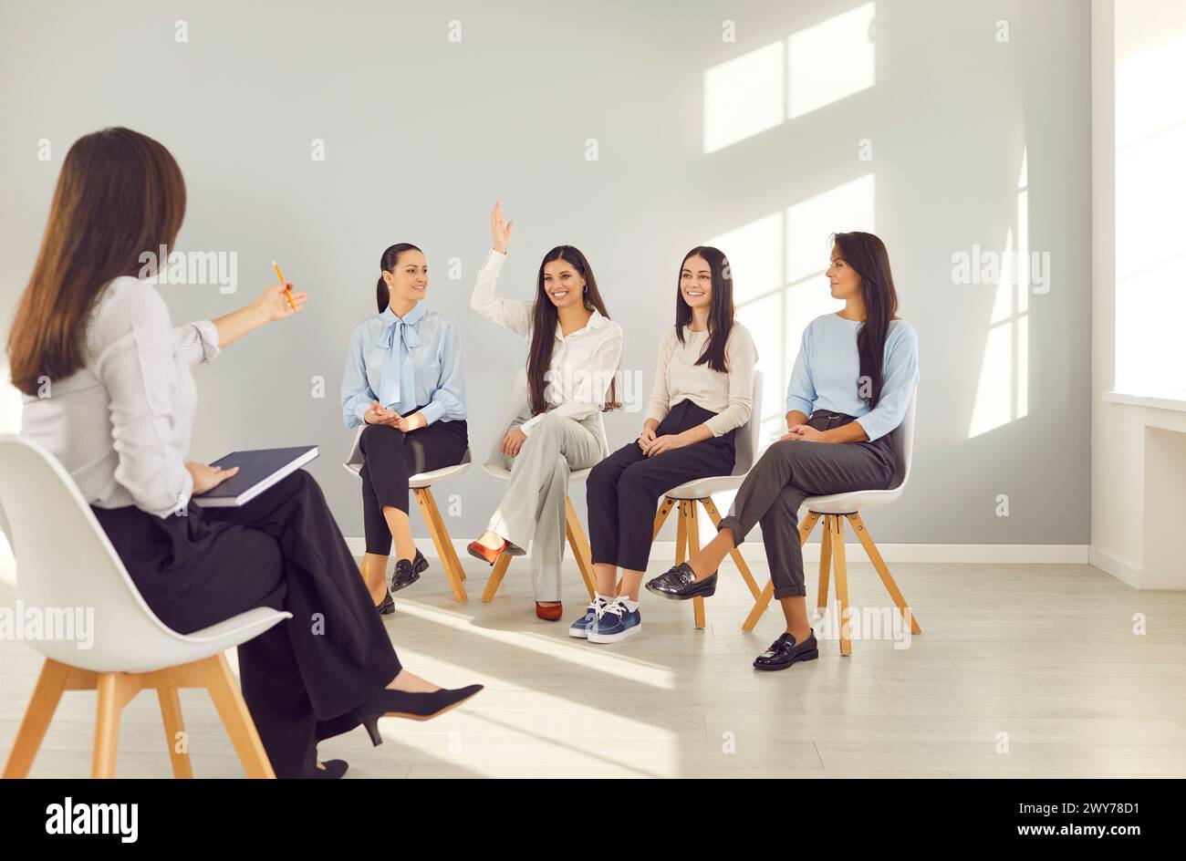 Group of young women group sitting in a row raising hand to ask or ...